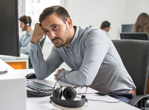 Lärm und schlechte Akustik im Büro und Callcenter Ein Mann sitzt gestresst und müde an seinem Arbeitsplatz im Büro ohne Schallschutz.