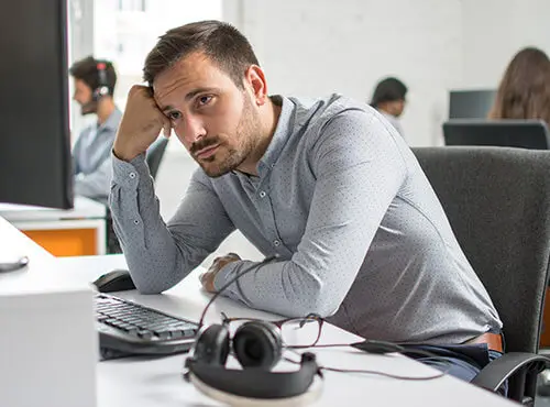 Ein Mann sitzt gestresst und müde an seinem Arbeitsplatz im Büro ohne Schallschutz.