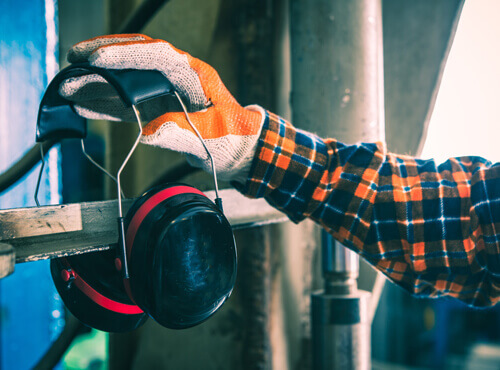 Gehörschutz und Schallschutz in der Industrie Ein Arbeiter greift zum Gehörschutz. um sich vor einer lauten Maschine zu schützen.