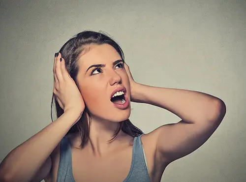 Ohne Schalldämmung: Eine Frau ist genervt durch den Lärm aus dem Heimkino Ihrer Nachbarn.