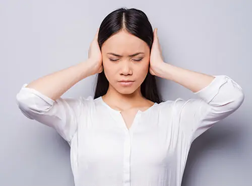 Eine junge Frau hält sich die Ohren zu, um Lärm zu vermeiden.