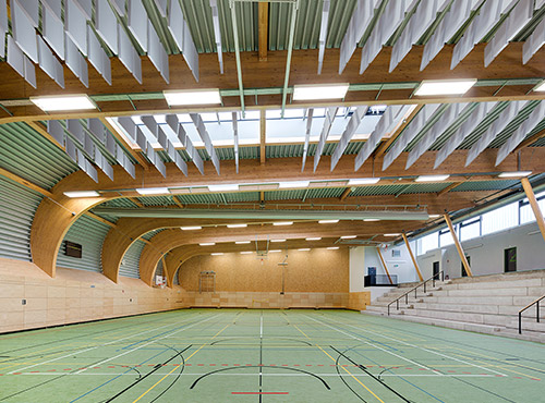Schallabsorber an der Decke einer Sporthalle Freischwebende Schallabsorber unter der Hallendecke einer Sporthalle senken den Lärmpegel und reduzieren Hall.