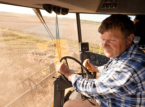 Schalldämmung von Landmaschinen und Forstmaschinen Weniger Lärm in der Landwirtschaft – ein Arbeiter fährt in einem schallgedämmten Mähdrescher.